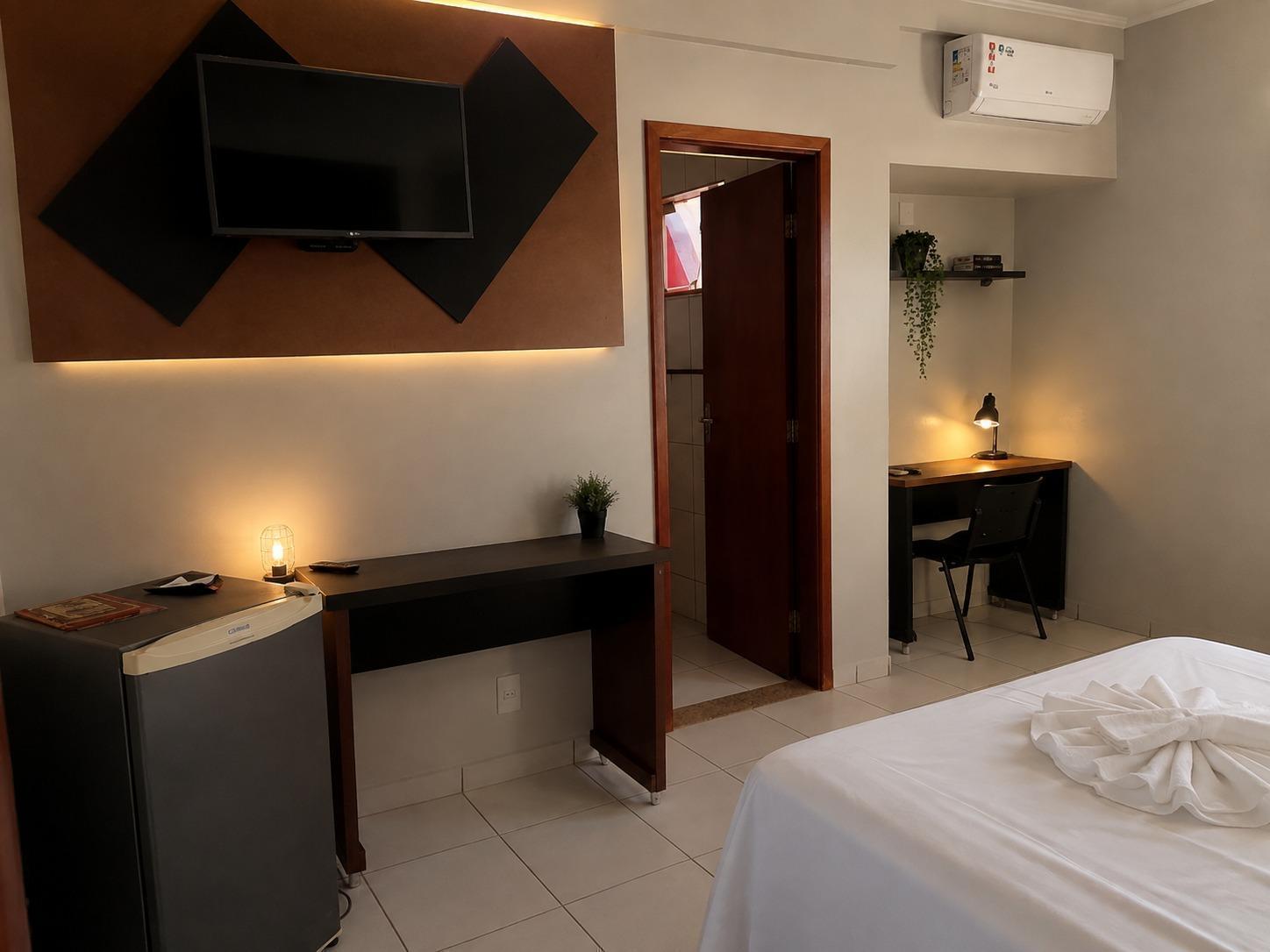 Quarto do Hotel Flor da Mata com TV na parede, frigobar, bancada de trabalho, ar-condicionado e cama de casal